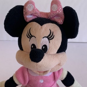 May include: A pink and black plush toy of Minnie Mouse wearing a pink bow with white polka dots and a pink dress with white polka dots.