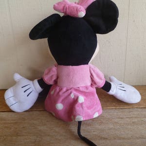 May include: A plush toy of Minnie Mouse wearing a pink dress with white polka dots and a pink bow. The toy has black ears and white gloves.