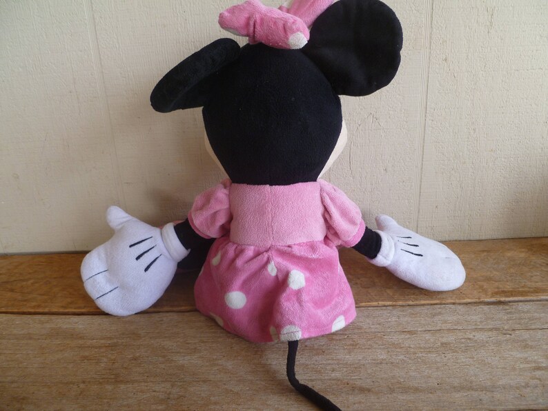 May include: A plush toy of Minnie Mouse wearing a pink dress with white polka dots and a pink bow. The toy has black ears and white gloves.
