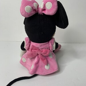 May include: A pink and black plush toy of Minnie Mouse. She is wearing a pink dress with white polka dots and a pink bow. She has a black tail and a black bow on her head.