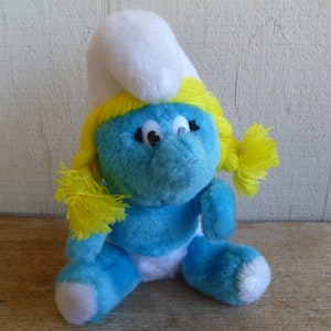 May include: A blue plush Smurf doll with a white hat and yellow hair. The doll has large, black eyes and a white diaper.