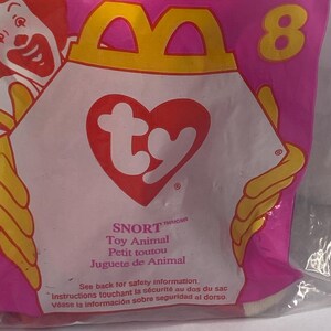以下が含まれることがあります： ピンク色のマクドナルドのバッグ。黄色と白のロゴがあり、数字の8が描かれています。バッグにはTy Snortのおもちゃの動物が入っています。バッグには英語、フランス語、スペイン語でテキストが書かれています。