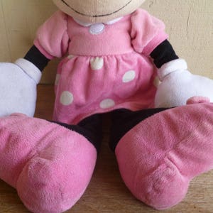 May include: A pink plush toy with white polka dots, black arms and legs, and a white collar. The toy is sitting with its legs crossed.