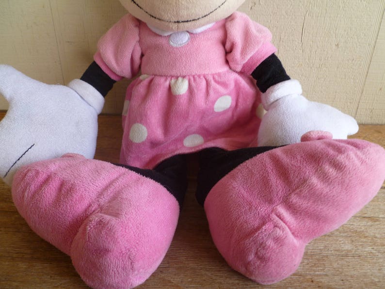 May include: A pink plush toy with white polka dots, black arms and legs, and a white collar. The toy is sitting with its legs crossed.