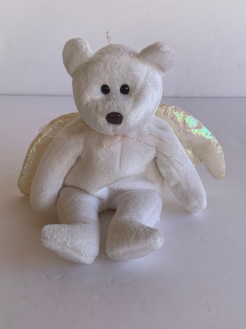 May include: White plush teddy bear with iridescent wings. The bear has black eyes and a brown nose. The wings are made of a sheer fabric with a shimmery finish.