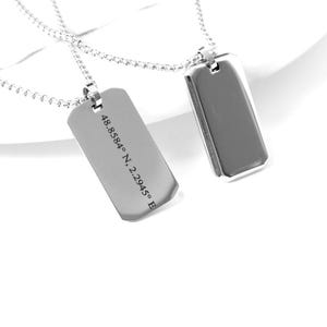 May include: Two silver dog tag necklaces. One tag has engraved coordinates: 48.8584° N, 2.2945° E. The tags are rectangular with rounded corners and hang on delicate silver chains. The background is white.
