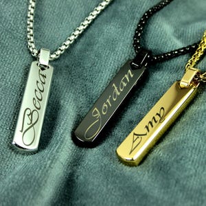 Op de afbeelding: Drie gepersonaliseerde kettingen met rechthoekige hangers. De hangers zijn gegraveerd met de namen "Becca", "Jordan" en "Amy". De kettingen zijn zilver, zwart en goudkleurig, elk met een bijpassende ketting.