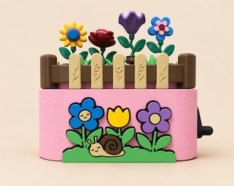 Peut inclure: Une boîte à musique rectangulaire rose présentant une scène de jardin avec un escargot souriant, de l'herbe verte et des fleurs colorées. Le dessus comporte une clôture en bois brun avec quatre fleurs en plastique jaune, rouge, violet et bleu.