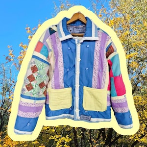 May include: A patchwork jacket with a blue, purple, and yellow color scheme. The jacket features a collared neckline, button closure, and two front pockets. The sleeves are a mix of patterned fabrics. The jacket is displayed against a backdrop of a blue sky and autumn foliage.