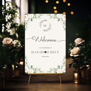 May include: A wedding welcome sign on a gold easel. The sign features floral accents and the names "David" and "Emily" with a heart symbol, along with the date. The word "Welcome" is written in elegant script.