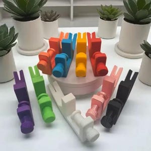 May include: A collection of colorful, small, adjustable tools in various colors, including purple, green, white, pink, black, red, orange, blue, and yellow. Each tool has a screw-like base and a forked top. The tools are arranged on a white surface.