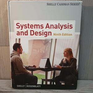 Könnte beinhalten: Ein Lehrbuch mit dem Titel "Systems Analysis and Design, Ninth Edition" von Shelly und Rosenblatt. Das Cover zeigt ein Foto von zwei Personen, die an einem Tisch mit einem Laptop sitzen. Das Buch gehört zur Shelly Cashman Series.