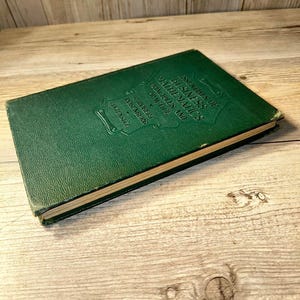 May include: A vintage green hardcover book titled "Essentials of Business Mathematics Principles and Practice" by R. Robert Rosenberg. The book is lying on a light-colored wooden surface. The book's cover has embossed text.
