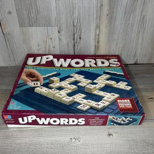 May include: A vintage Upwords board game. The box is red and blue, with the game title prominently displayed. The game board is dark blue, with beige letter tiles. The text on the box reads "The 3-Dimensional Word Game That Really Stacks Up!"