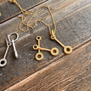 Peut inclure: Plusieurs colliers et pendentifs en or et en argent. Les colliers en or présentent un design linéaire avec des accents circulaires. Le collier en argent a un design similaire. Les bijoux sont présentés sur une surface en bois rustique.