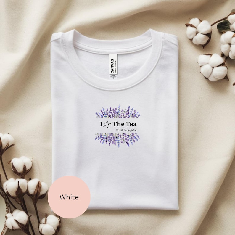 May include: White t-shirt with a crew neck. The shirt features the text "I Am The Tea" in black, surrounded by a lavender floral design. The text "-Violet Bridgerton" is below the main text. A pink circle with the word "White" is in the lower left.