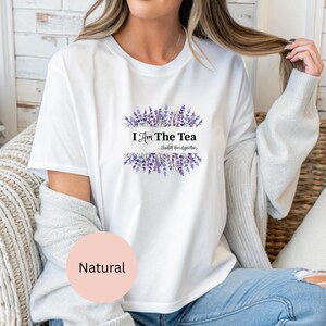 May include: White t-shirt with the text "I Am The Tea...Violet Bridgerton" in black font, framed by purple lavender sprigs. The shirt is a natural color and has short sleeves.