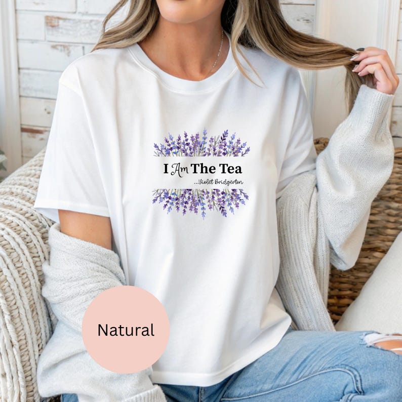 May include: White t-shirt with the text "I Am The Tea...Violet Bridgerton" in black font, framed by purple lavender sprigs. The shirt is a natural color and has short sleeves.