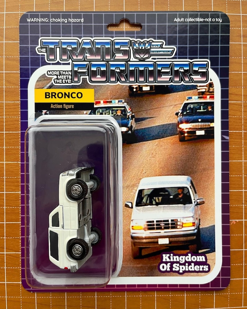 May include: A white toy car with the words "Kingdom of Spiders" printed on the bottom of the card. The car is a Ford Bronco and is part of a Transformers toy line. The card has a warning label that says "choking hazard" and "adult collectible - not a toy".