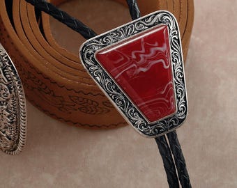 Könnte beinhalten: Eine Bolo-Krawatte mit einem rot-weiß marmorierten Steinanhänger, der in einen silberfarbenen Rahmen mit einem verzierten Design gefasst ist. Die Krawatte hat eine schwarze geflochtene Kordel.