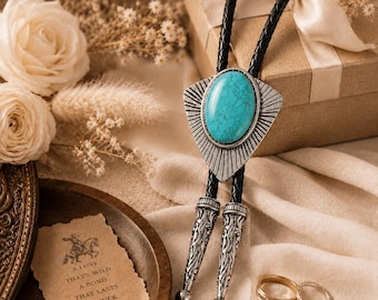 May include: A bolo tie featuring a large oval turquoise stone set in a silver-toned triangular metal plate with radiating lines. The black braided cord ends in two silver-toned metal tips with intricate engraved patterns and rounded ends.