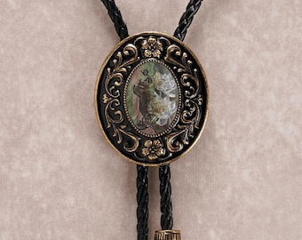 May include: An oval bolo tie with a black braided leather cord. The decorative centerpiece features a black and gold filigree design around an oval mother-of-pearl inlay with a floral and animal motif.