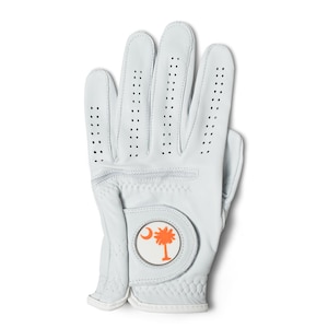 Puede incluir: Guante de golf blanco con un logotipo de palmera y media luna. El guante tiene pequeños orificios de ventilación y una zona de agarre texturizada. El logotipo es naranja y blanco. El guante es de cuero.