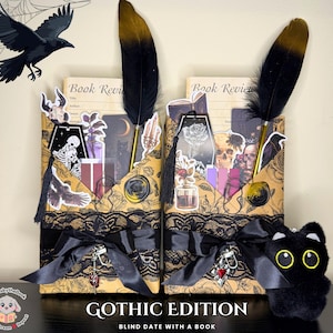 May include: Two Gothic-themed book holders with black lace, bows, and decorative stickers. Each holder features a black and gold feather pen. The text "GOTHIC EDITION" and "BLIND DATE WITH A BOOK" are visible. A black cat plushie with yellow eyes is also present.