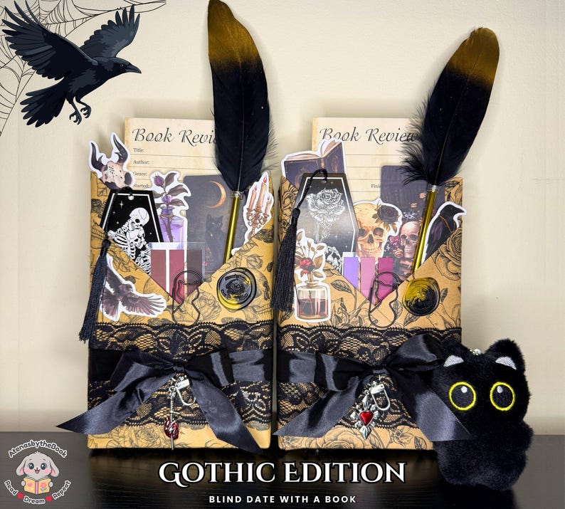 May include: Two Gothic-themed book holders with black lace, bows, and decorative stickers. Each holder features a black and gold feather pen. The text "GOTHIC EDITION" and "BLIND DATE WITH A BOOK" are visible. A black cat plushie with yellow eyes is also present.