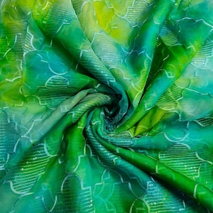 May include: A vibrant, flowing fabric in shades of green and yellow. The material features a delicate, repeating pattern of white embroidered shapes. The fabric is draped and swirled, showcasing its texture and color variations.