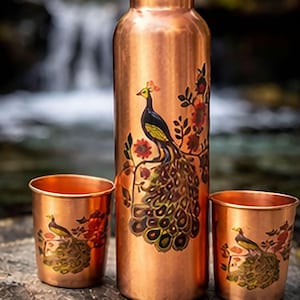 Puede incluir: Botella de agua de cobre y dos tazas a juego, todas adornadas con un diseño de pavo real. El pavo real se representa con un cuerpo negro, cabeza amarilla y una cola vibrante y detallada, sobre un fondo de flores.