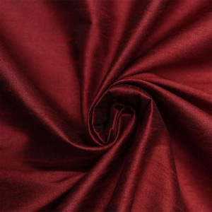 Pode incluir: Close-up de um tecido bordô profundo com um brilho sutil. O material é tecido firmemente, com textura visível e dobras que criam sombras. O tecido é reunido em espiral, destacando sua queda e cor.