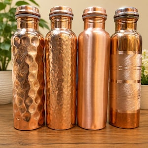 May include: Four cylindrical copper water bottles standing in a row. The first two bottles feature a hammered texture, the third has a smooth polished finish, and the fourth displays a horizontal brushed pattern. Each bottle has a matching metal cap.