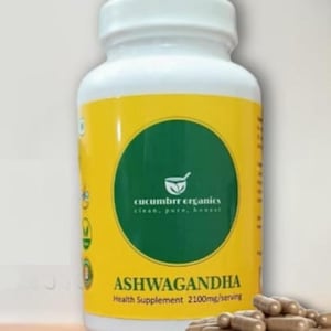 May include: A white bottle of Ashwagandha health supplement with a yellow label and a green circle logo. The label includes the text "CUCUMBRR ORGANICS" and "ASHWAGANDHA". Brown capsules are in front of the bottle.