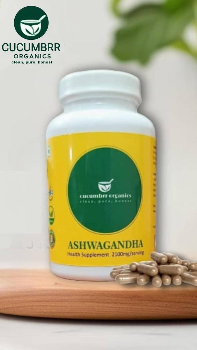 May include: A white bottle of Ashwagandha health supplement with a yellow label and a green circle logo. The label includes the text "CUCUMBRR ORGANICS" and "ASHWAGANDHA". Brown capsules are in front of the bottle.