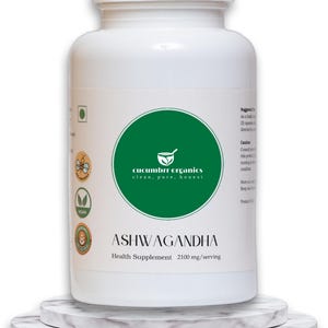 May include: A white bottle of Ashwagandha health supplement. The bottle has a green circular label with the text "cucumber organics clean, pure, honest". The label also includes the text "ASHWAGANDHA Health Supplement 2100 mg/serving". The bottle is on a marble stand.