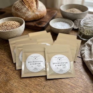 May include: Multiple small, rectangular, brown paper pouches containing sourdough starter. Each pouch features a circular white label with the text THE MIDNIGHT BAKER, SOURDOUGH STARTER, 15g, and a small illustration of a loaf of bread.