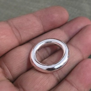 May include: A shiny, silver-colored ring with a smooth, rounded design. The ring has a circular shape with a hollow center. The ring is shown in a close-up view, highlighting its polished surface and reflective qualities.