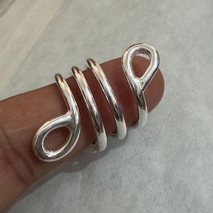 Può includere: Un anello a spirale color argento dal design unico. L'anello presenta una serie di anelli e curve, creando un'estetica accattivante e moderna. L'anello è mostrato su un dito, evidenziando la sua forma e il suo stile.