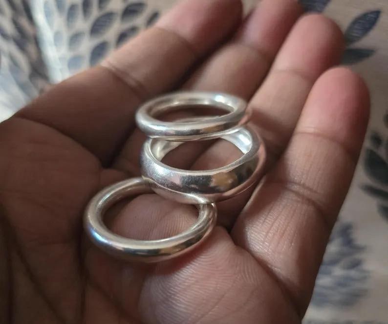 Pu&ograve; includere: Tre anelli d'argento di diverse larghezze sono mostrati in una mano. Gli anelli hanno una finitura liscia e lucida, che riflette la luce. Gli anelli sono probabilmente in metallo e hanno un design semplice e classico.