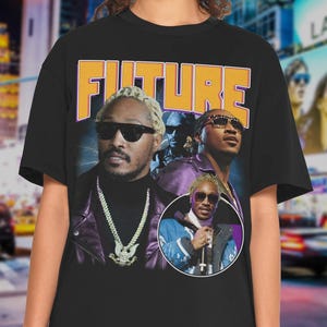 May include: Black t-shirt featuring a graphic of the word "FUTURE" in orange and white block letters. The graphic includes multiple images of a man wearing sunglasses and jewelry. The shirt is a classic crew neck style.