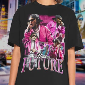 May include: Black t-shirt featuring a collage of images of a person wearing sunglasses and a pink jacket, holding a microphone. The text "Hendrix FUTURE" is displayed in pink, stylized lettering.