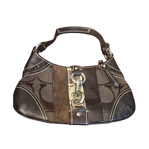 May include: Brown shoulder bag with a curved shape. The bag features a combination of textures, including leather, suede, and a patterned fabric. It has a silver-tone clasp and a handle. White stitching accents the edges.