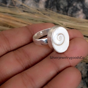 May include: A silver ring featuring a white, oval-shaped stone with a spiral pattern. The text "SilverjewelrygoodsCo" is visible at the bottom right of the image.