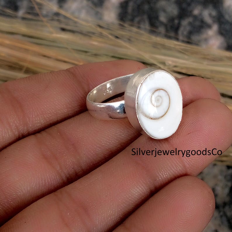 May include: A silver ring with a white oval-shaped centerpiece. The centerpiece has a spiral design. The text "SilverjewelrygoodsCo" is visible at the bottom right of the image.