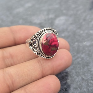 Könnte beinhalten: Ein silberner Ring mit einem ovalen, rot-goldenen Stein. Der Ring hat ein verziertes Design mit Perlen- und Schnörkeldetails um den Stein. Der Stein hat ein marmoriertes Aussehen mit Rot-, Rosa- und Goldtönen.
