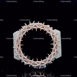 May include: A rose gold and silver bracelet with a crown of thorns design. The bracelet features sharp, pointed thorns and is encrusted with small, sparkling stones. The background is black, highlighting the jewellery.