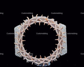 May include: A rose gold and silver-toned bracelet with a crown of thorns design. The bracelet features a series of sharp, pointed thorns and is encrusted with small, sparkling stones. The background is black, highlighting the jewelry.