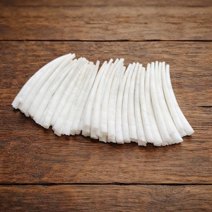 Puede incluir: Un conjunto de objetos blancos, delgados y curvos, posiblemente alimentos, dispuestos sobre una superficie de madera marrón oscura. Los objetos tienen un aspecto ligeramente texturizado y están espaciados uniformemente.