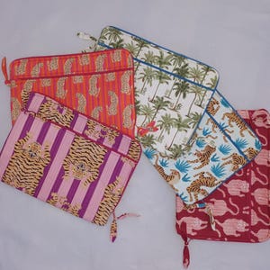 Könnte beinhalten: Eine Auswahl an Laptop-Hüllen mit verschiedenen Tier- und Tropenmustern. Designs umfassen orangefarbene Leopardenmuster, rosa Tigerstreifen, Palmen und rote Tiersilhouetten. Jede Hülle hat einen Reißverschluss und einen kleinen Griff.